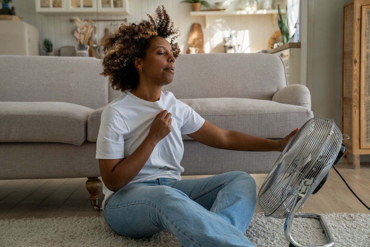 Woman sits in front of a fan to cool herself